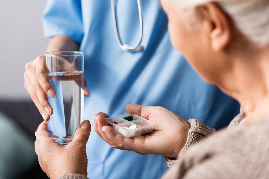stock-photo-partial-view-nurse-giving-pills-glass-water-elderly-woman-selective-1